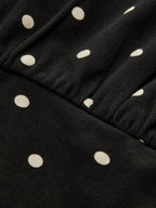 Black batwing top with off-white polka dots, diagonal ribbing, crew neck, cinched waist.