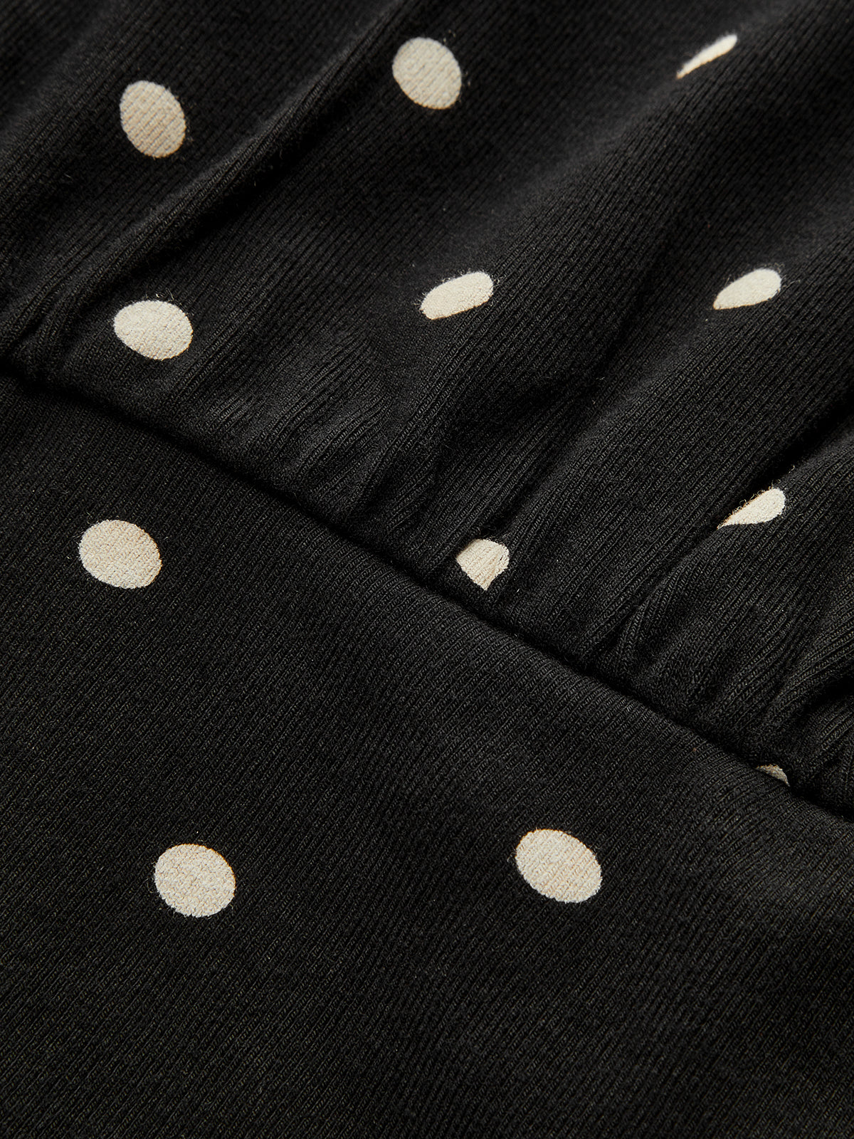 Black batwing top with off-white polka dots, diagonal ribbing, crew neck, cinched waist.
