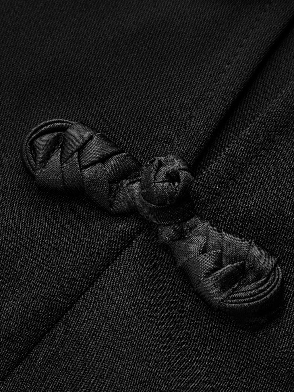 Close-up of a Mandarin collar dress featuring intricate black frog button knots on smooth fabric.