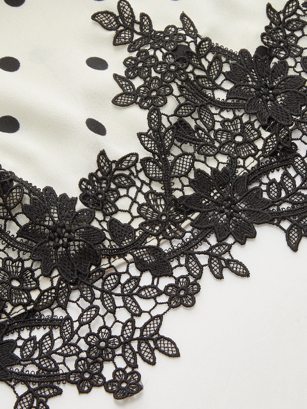 White ruched sleeveless top with black polka dots and detailed black floral lace hem.