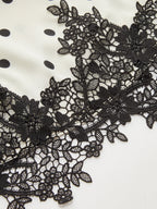 White ruched sleeveless top with black polka dots and detailed black floral lace hem.