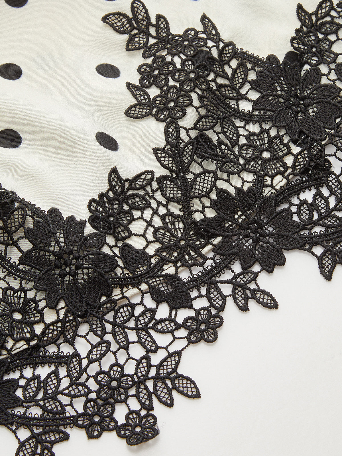 White ruched sleeveless top with black polka dots and detailed black floral lace hem.