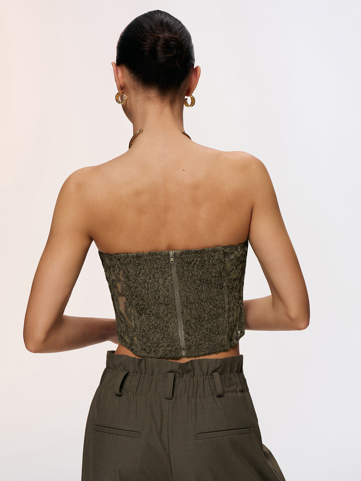 LA FINE FLEUR Romantic Lace Strapless Bustier Top paired with high-waisted olive green pants.