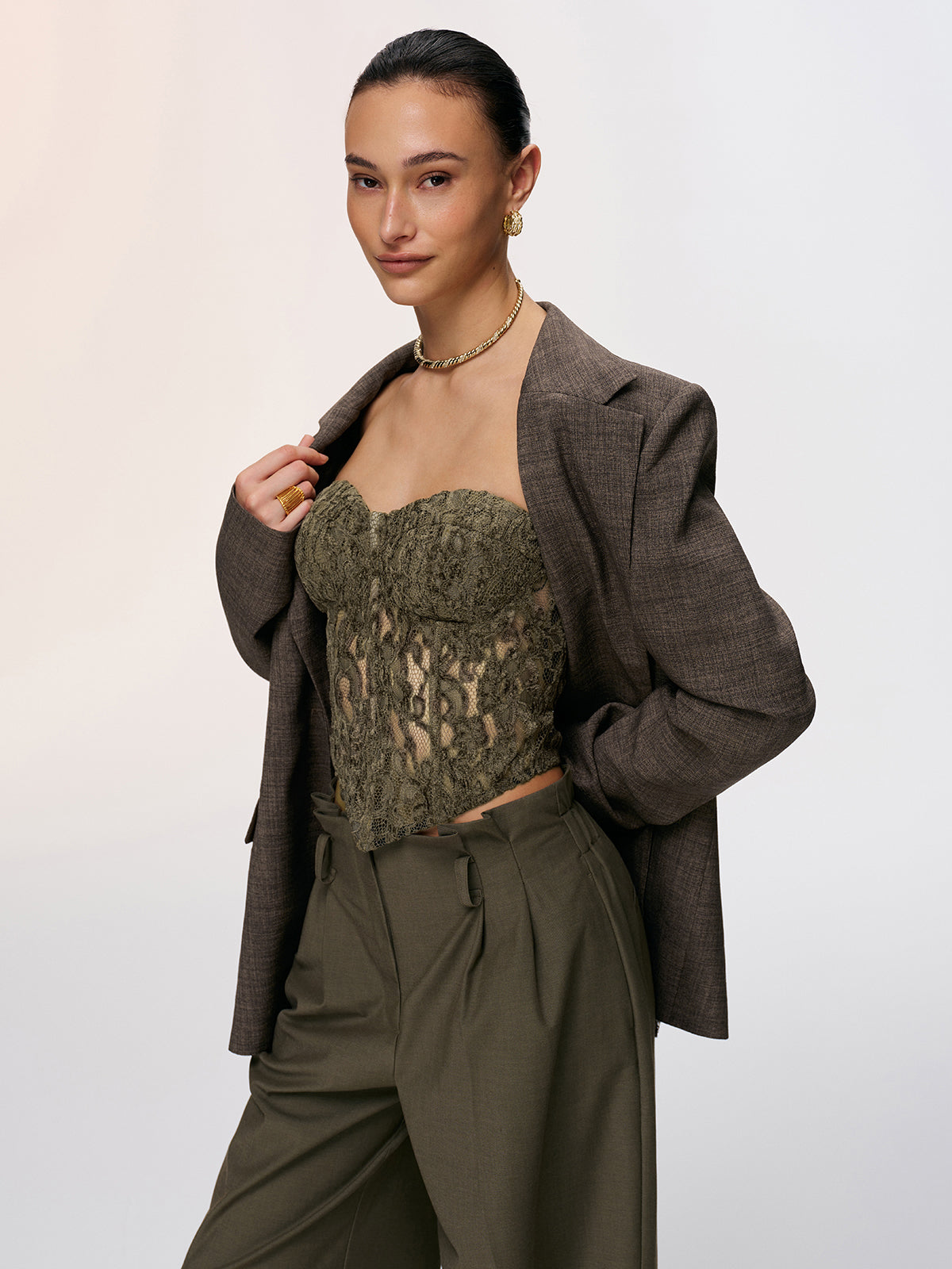 A strapless lace bustier top, high-waisted olive pants, and a brown draped blazer.