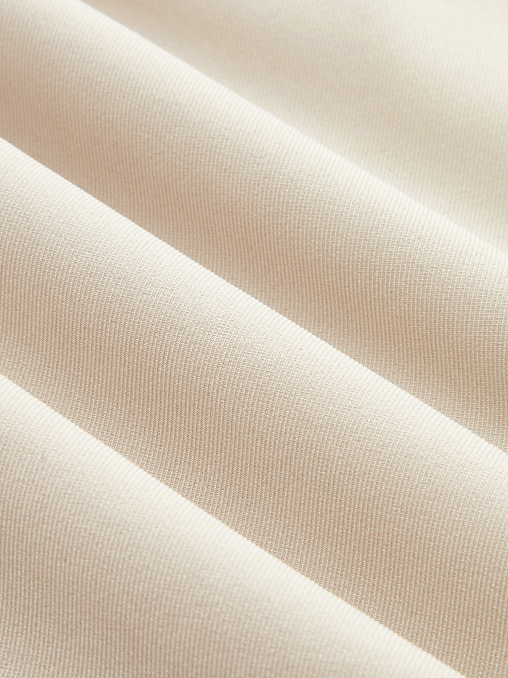 Light beige, ribbed fabric romper with smooth texture and parallel ridges in close-up.