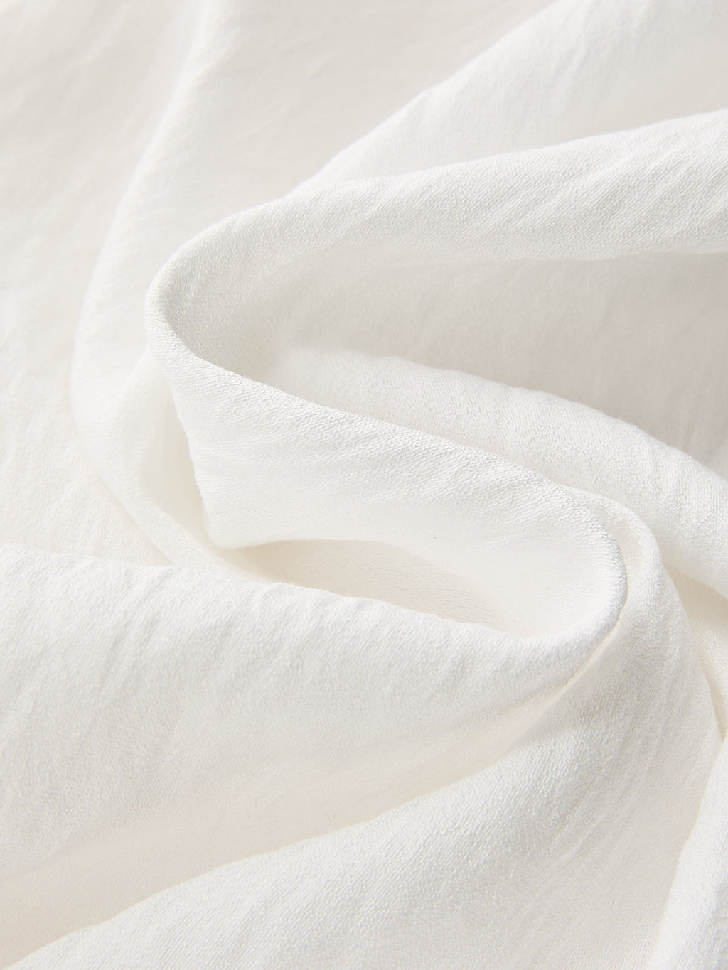 Soft white crop top with gentle folds and subtle texture, paired with patterned pants.