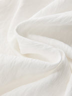 Soft white crop top with gentle folds and subtle texture, paired with patterned pants.