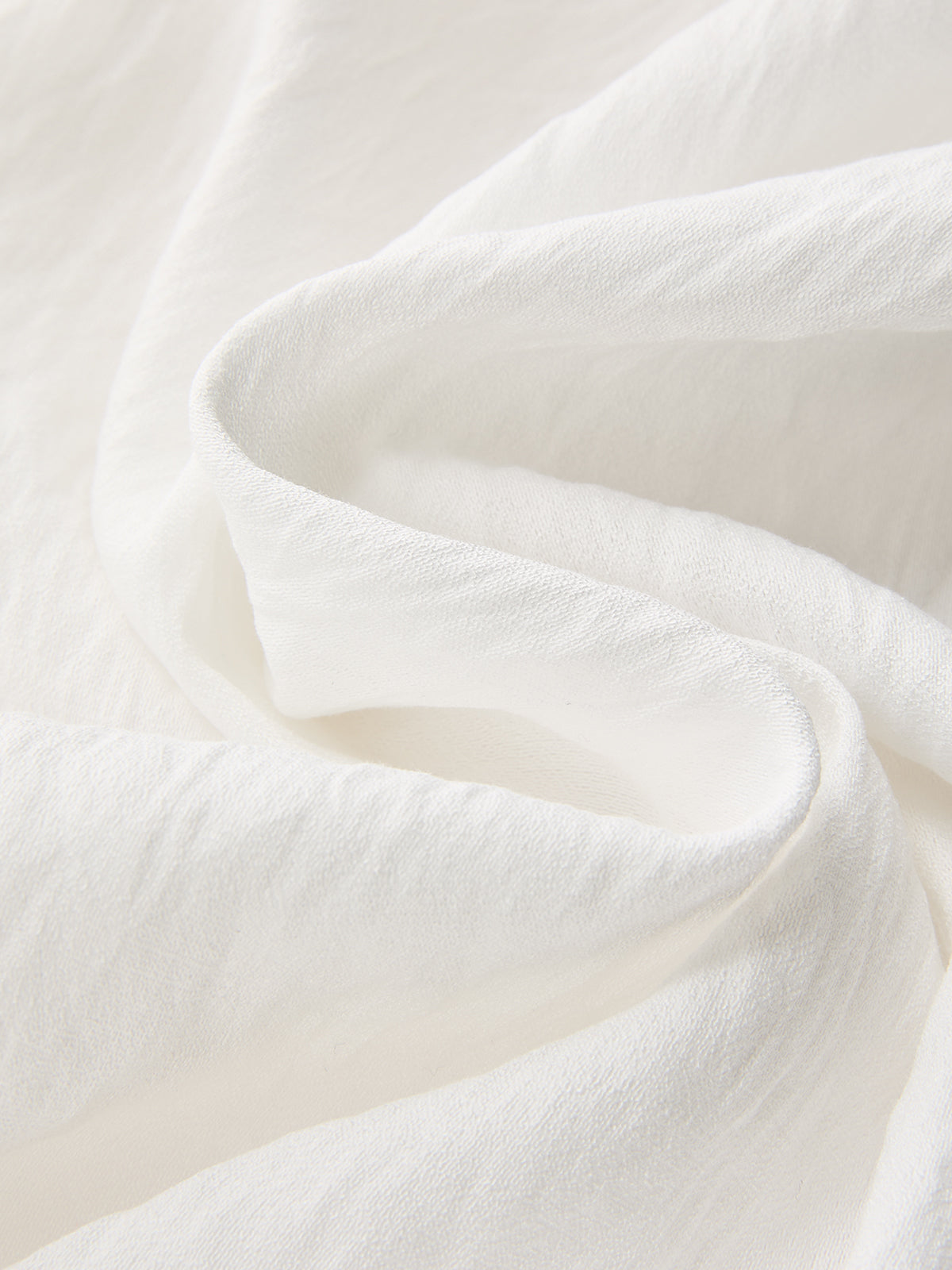 Soft white crop top with gentle folds and subtle texture, paired with patterned pants.