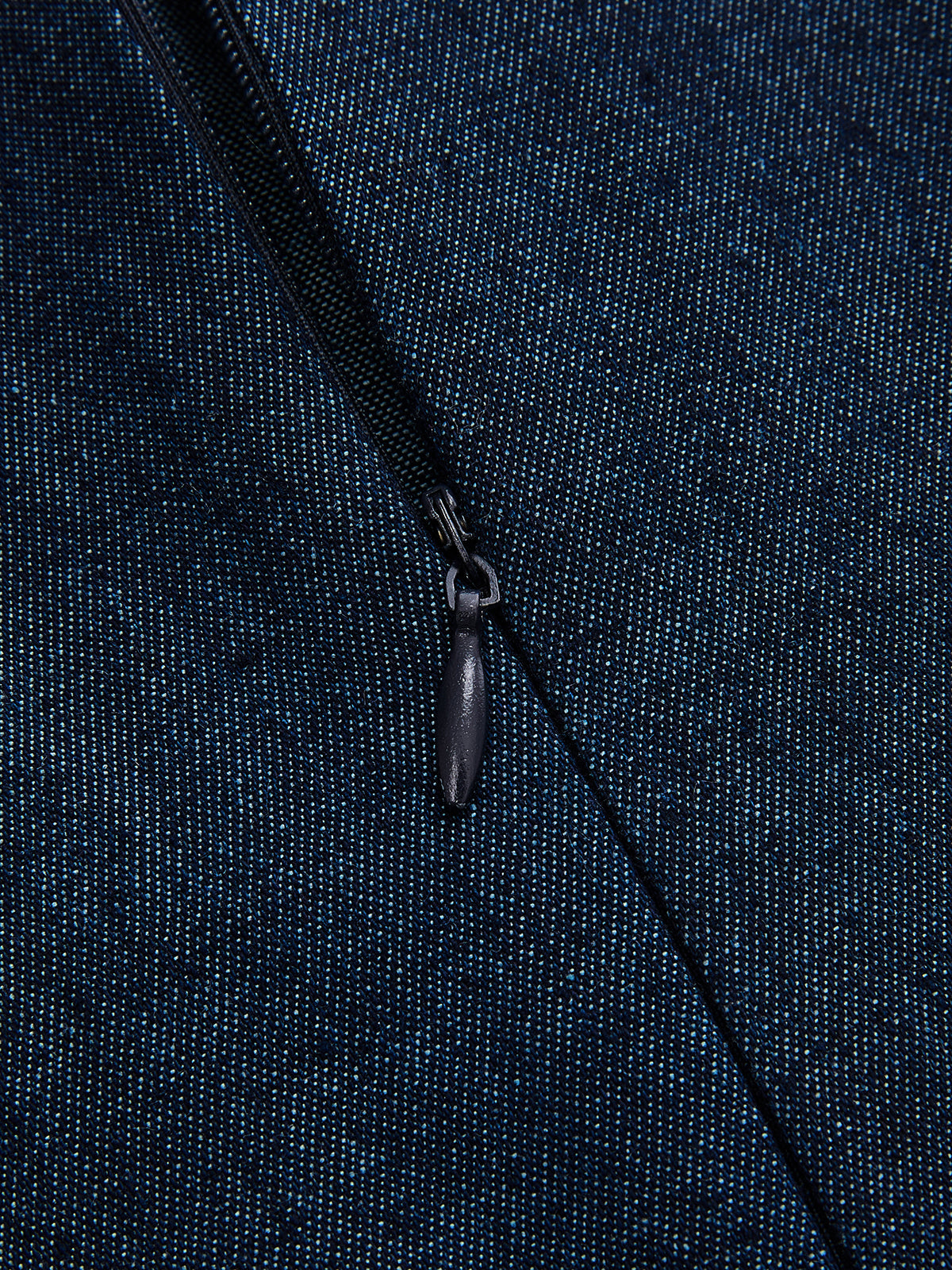 Close-up of a partially unzipped black zipper on a dark blue, speckled denim dress.