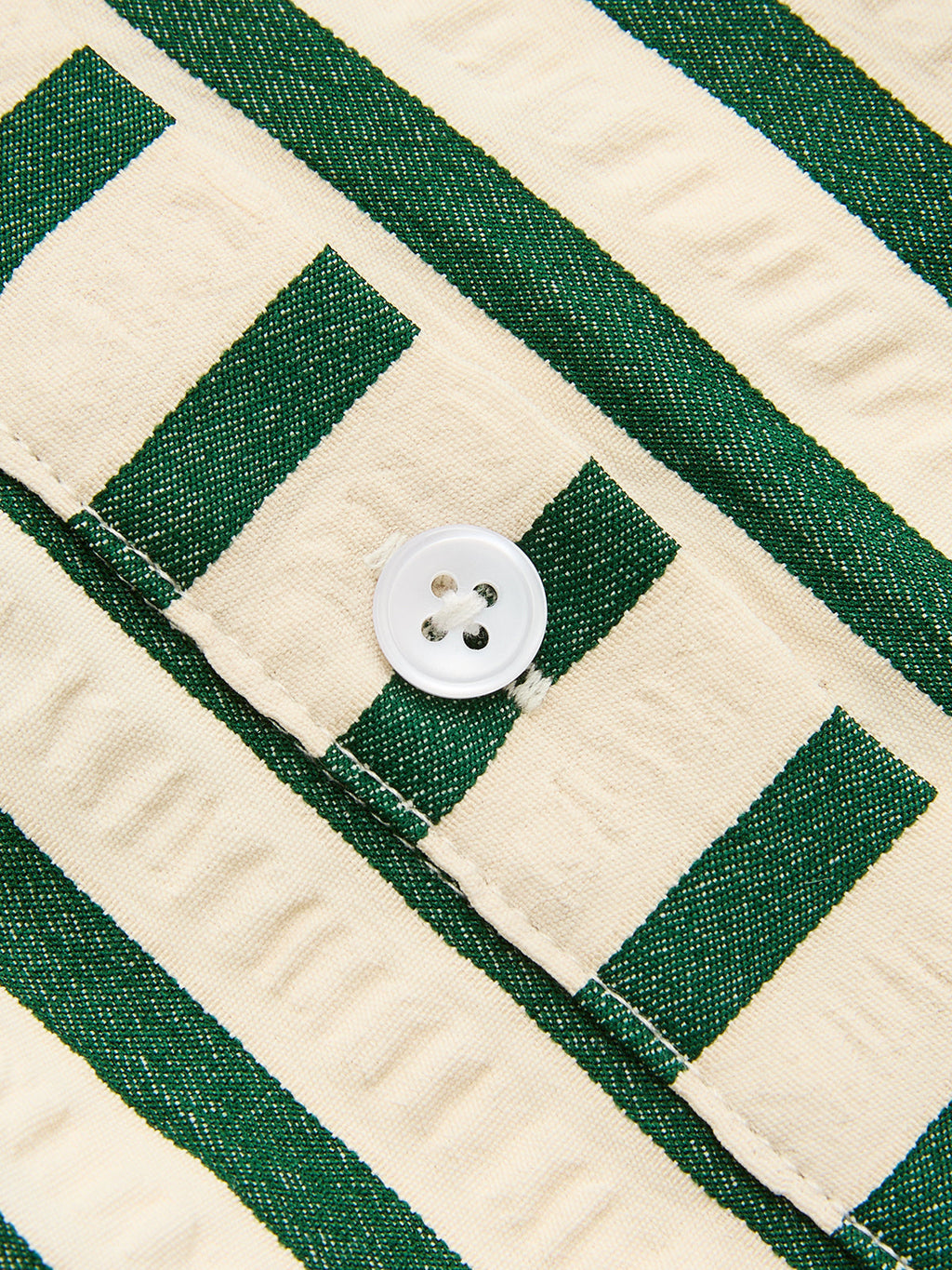 Textured woven polyester dress with cream and green stripes, white button, and partial buttonhole.