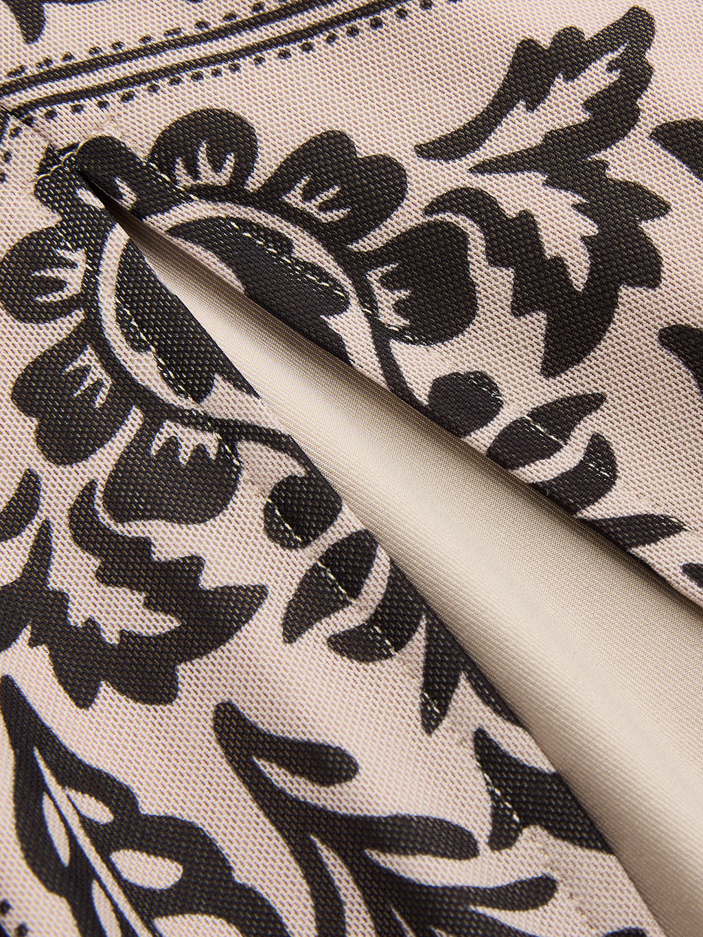 Beige flowy sleeveless maxi dress with black floral pattern, lined pocket, and neat stitching.