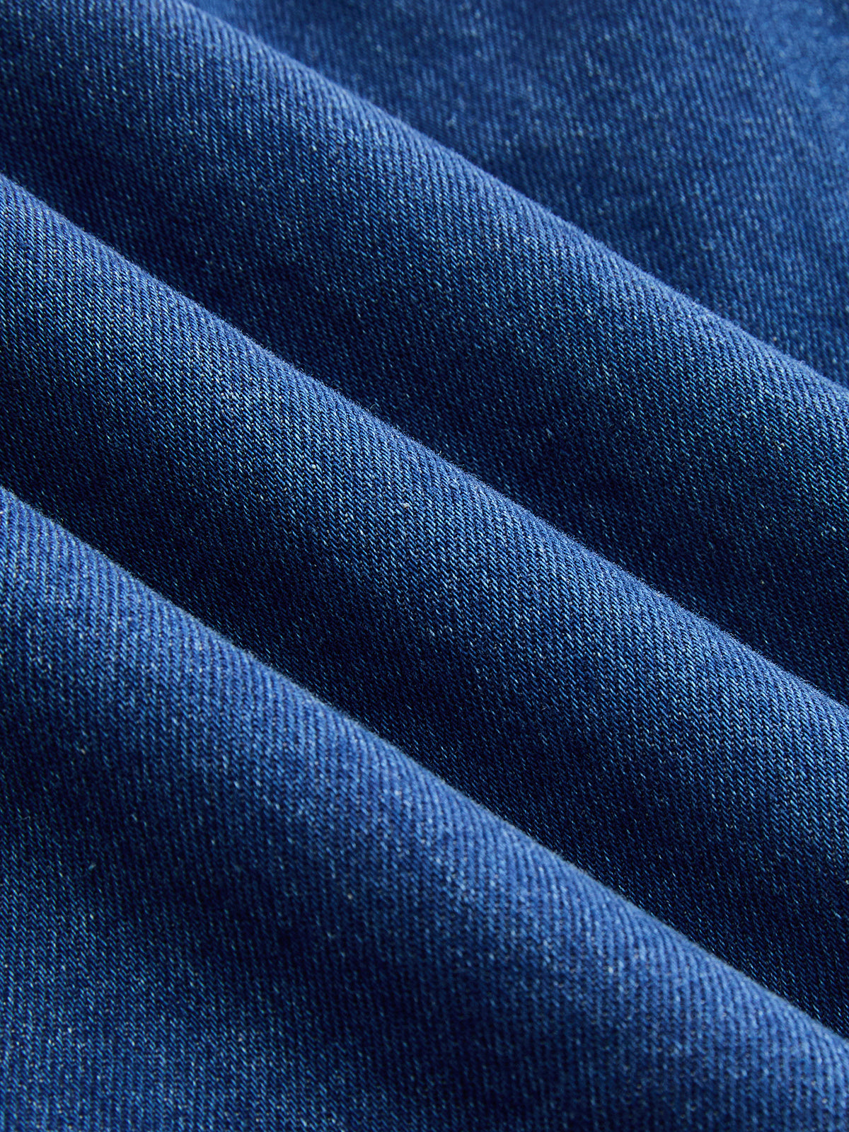 Close-up of indigo cotton-blend denim sleeveless mini dress with diagonal weave and soft folds.