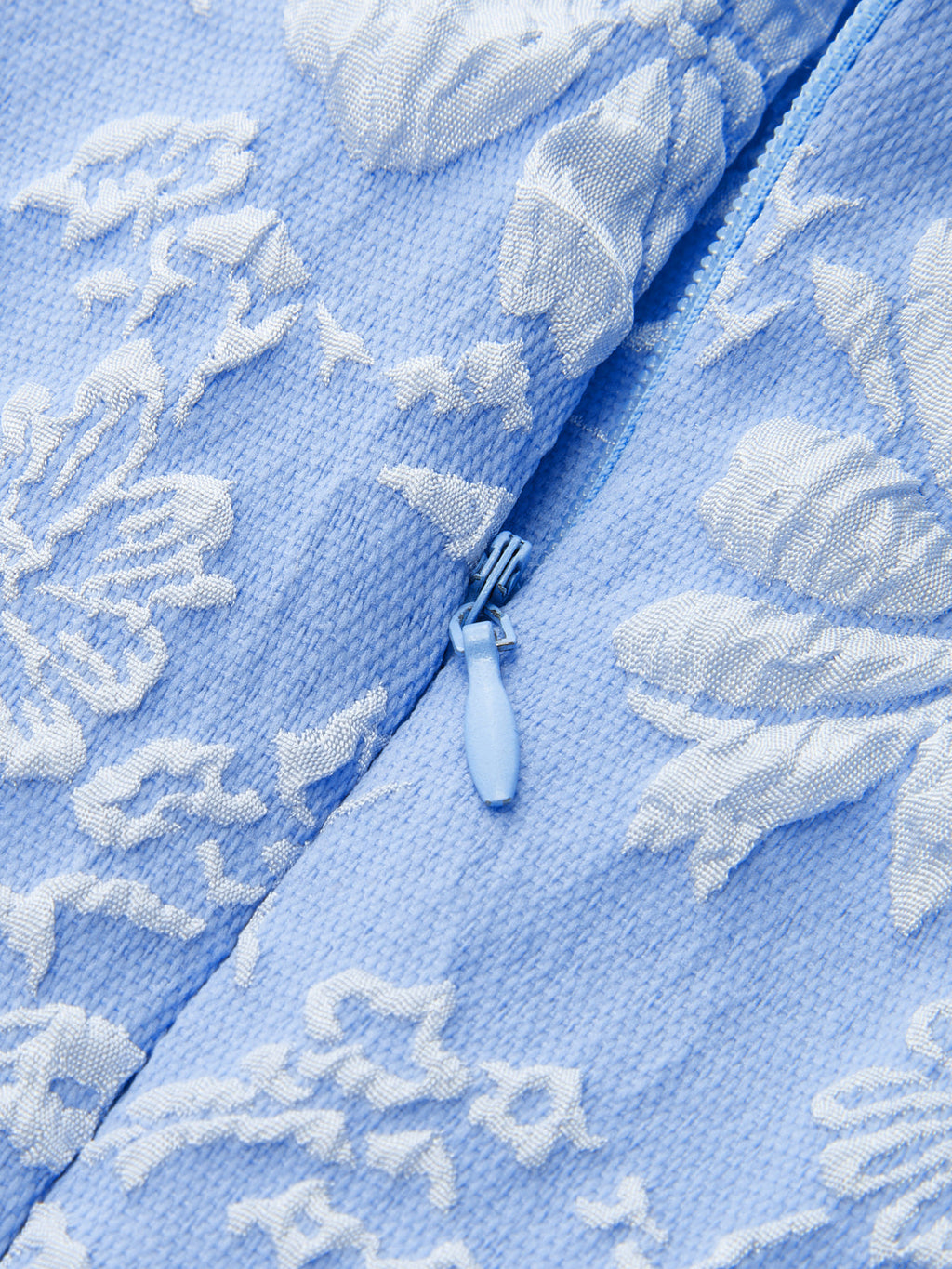 Sleeveless mini dress with white floral jacquard, slim fit, and central blue zipper.