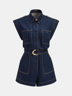Sleeveless denim romper with wide shoulders, chest pockets, gold-buckle belt, and bold stitching.