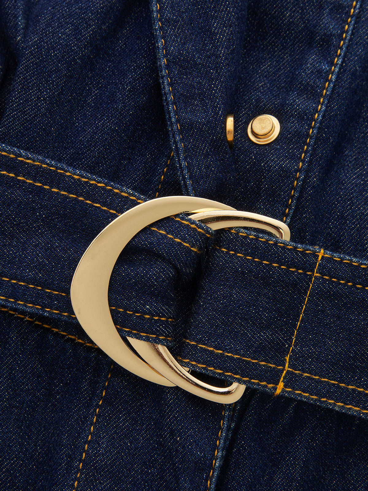 Sleeveless denim romper with gold buckle, yellow stitching, and epaulet details on the belt.