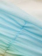 Gradient light blue and white mesh evening gown with diagonal ruching and pleated, semi-transparent textures.